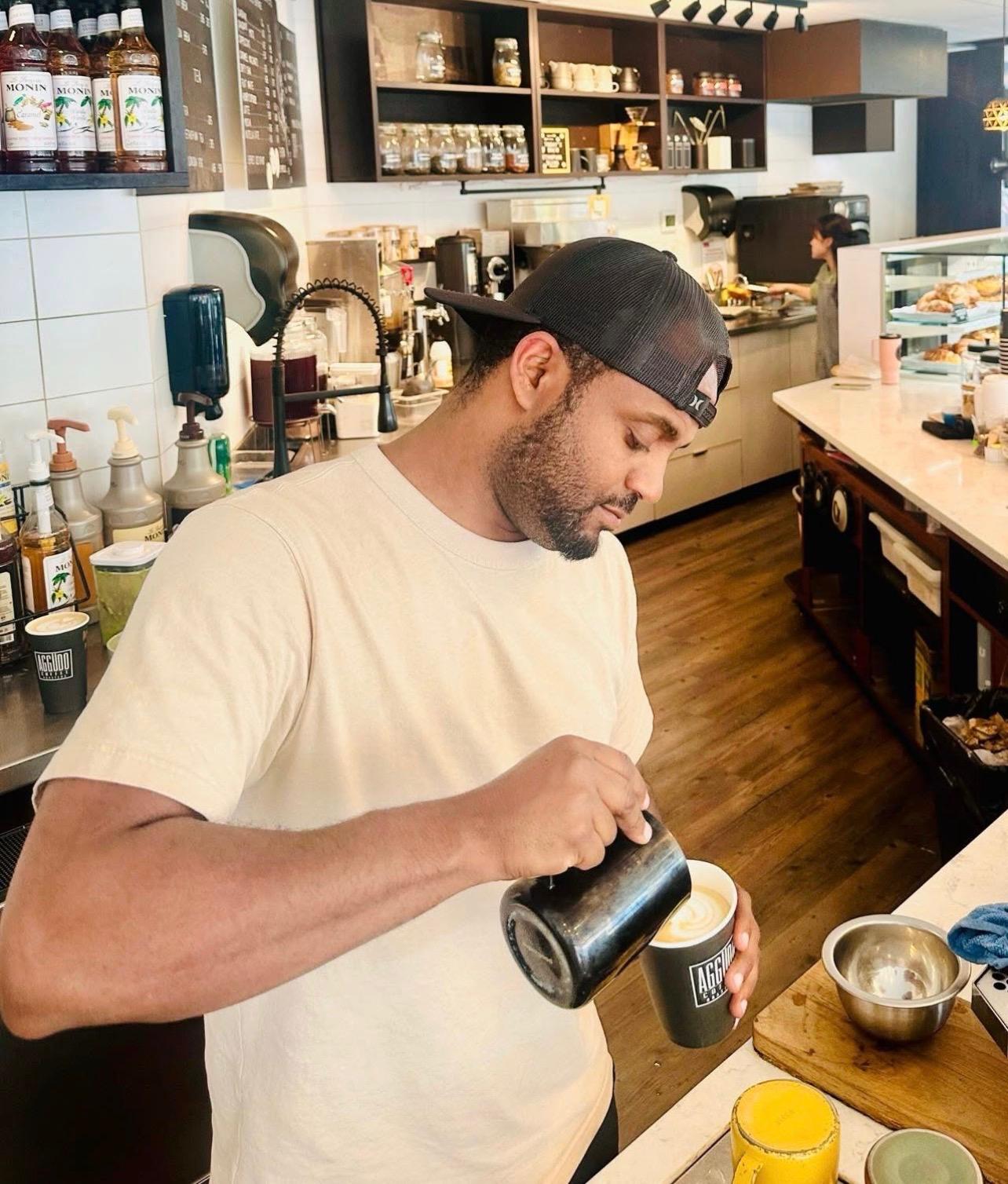 Bini pouring latte art into an Aggüdo cup behind the bar